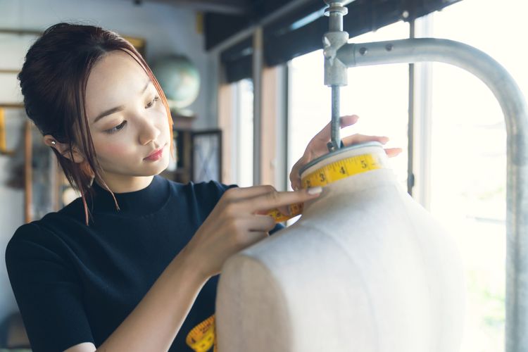 女子正在針對人形模特兒量尺寸裁縫