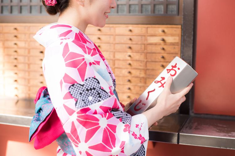 A Japanese woman in a kimono gets an omikuji fortune